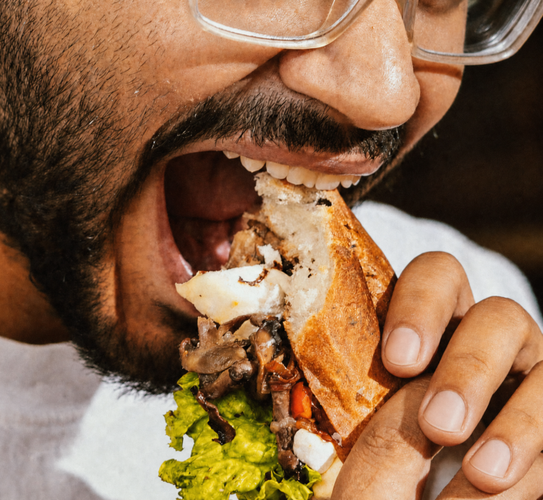 Man biting into a large sandwich, illustrating jaw fatigue while chewing