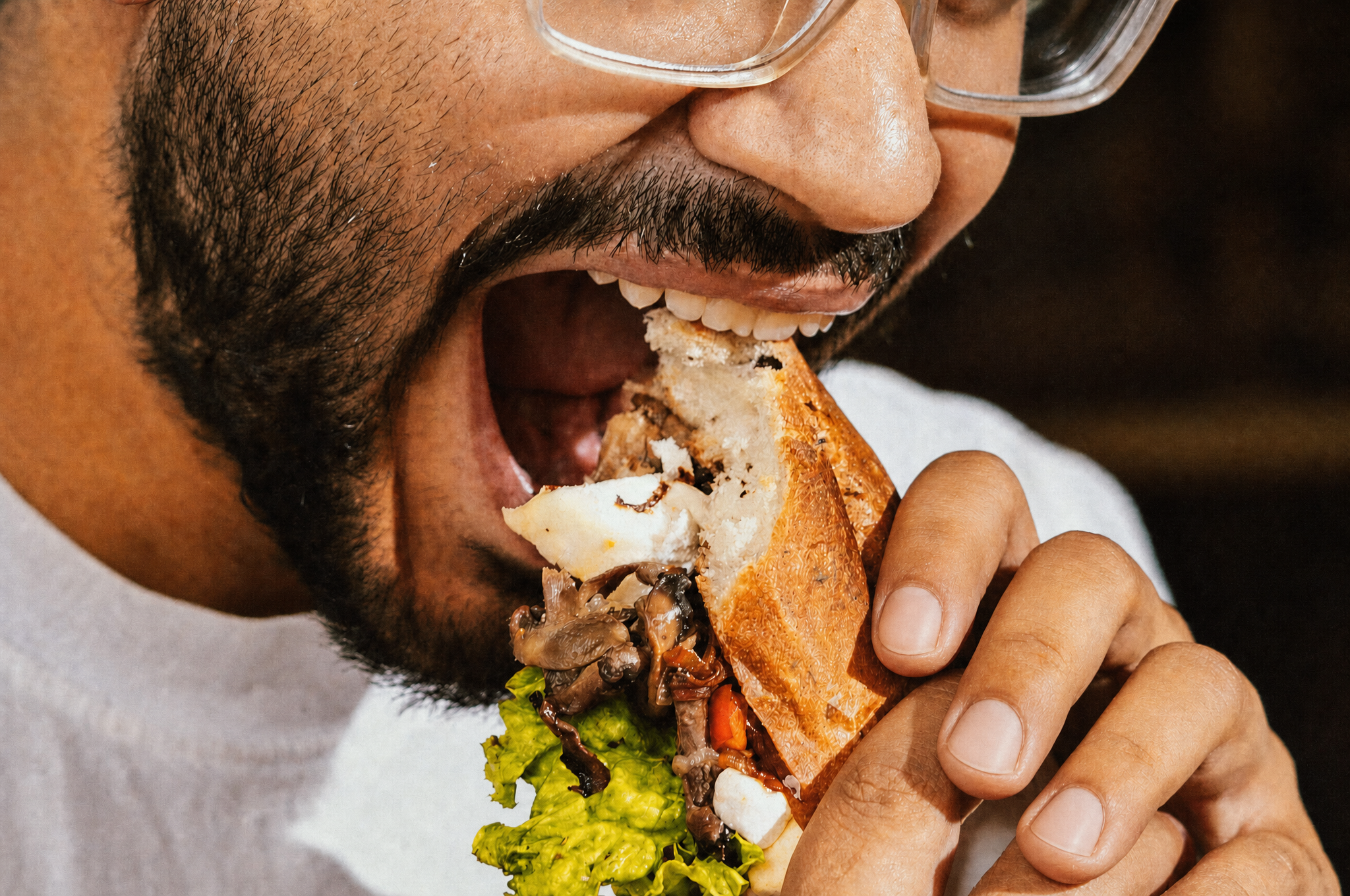 Man biting into a large sandwich, illustrating jaw fatigue while chewing